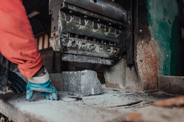 A worker in heavy industry breaks stone blocks using large machines. Granite and stone processing industry.