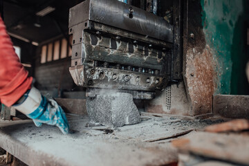 A worker in heavy industry breaks stone blocks using large machines. Granite and stone processing industry.