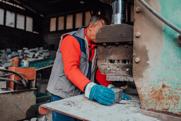 A worker in heavy industry breaks stone blocks using large machines. Granite and stone processing industry.