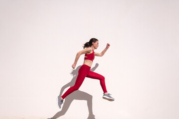 Fototapeta na wymiar Sporty female running and jumping outdoors against a white wall.
