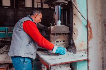 A worker in heavy industry breaks stone blocks using large machines. Granite and stone processing industry.