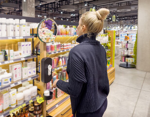 Woman buying make up at cosmetics section in store. choosing cosmetics, perfumes, creams and shampoos, Using tester.