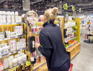 Woman buying make up at cosmetics section in store. choosing cosmetics, perfumes, creams and shampoos, Using tester.