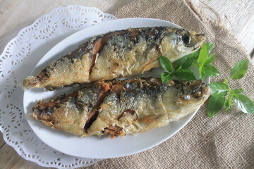 Indonesian cuisine called fried milkfish in a white plate on a wooden table