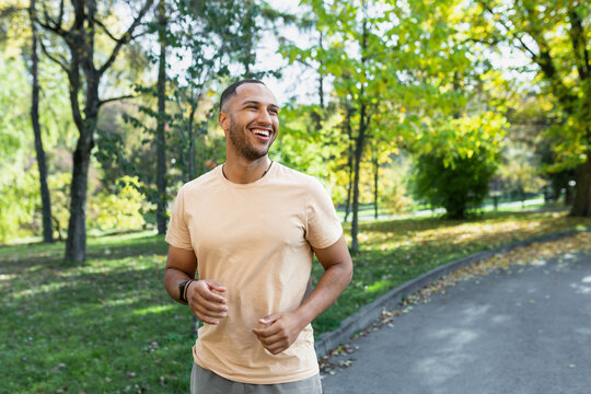 Cheerful and successful hispanic man jogging in the park, man running on a sunny day, smiling and happy having an outdoor activity.