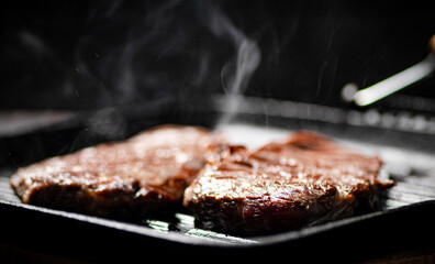 Cooking grilled steak in a frying pan with hot steam. 