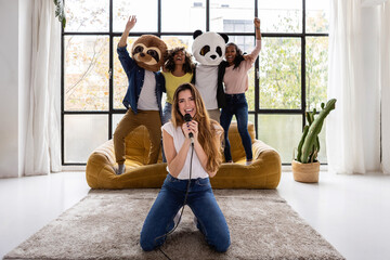 Vertical shot of young group of multiracial student friends having fun playing karaoke together at home party - obrazy, fototapety, plakaty