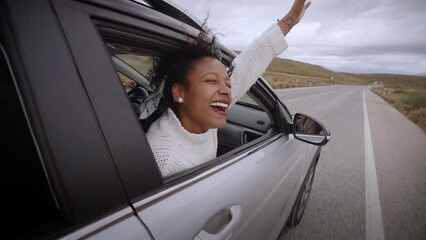 Latin smiling woman in car window. Automobile trip. Curly hair in wind. Girl looks out of auto window. Young female enjoying the view from the automobile on a secondary road. Slow motion. Freedom.