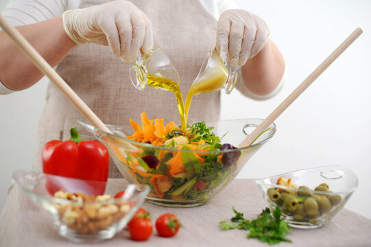 cook in sterile gloves prepares delicious healthy food pour dressing into salad in glass bowl from two jugs stream of salad olive oil and sauce with mustard and honey ingredients