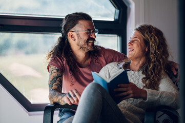 Man is embracing his girlfriend while she is reading a book at home