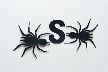 the letter S with black paper spider glyph cutouts on white paper