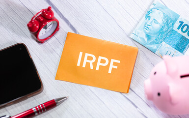 A sigla IRPF de Imposto de Renda da Pessoa Física escrita em um pedaço de papel que está sobre...