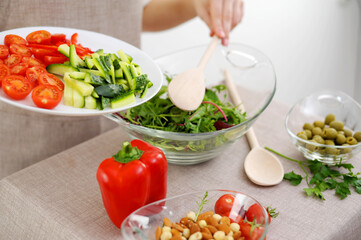 close-up of salad kneading with wooden spoons cherry tomatoes cocktail cucumbers olives and other ingredients lie on table with beige tablecloth beige apron restaurant food serving table setting