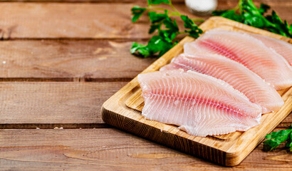 Raw fish fillet with parsley on a cutting board. 