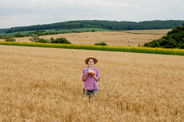 Naklejka na ściany i meble A woman farmer holds organic grain bread in her hands on the background of a wheat field. Bread is life