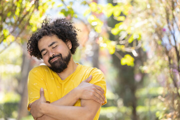 Naklejka na ściany i meble young Mexican man with beard and afro hugging himself, self love concept