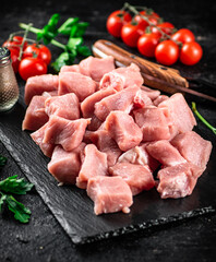 Pieces of raw pork on a stone board with parsley, tomatoes and spices. 