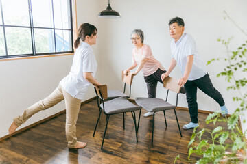 介護施設で椅子体操・運動・リハビリするシニア・高齢者の男女と理学療法士・介護士・トレーナー（脚）
