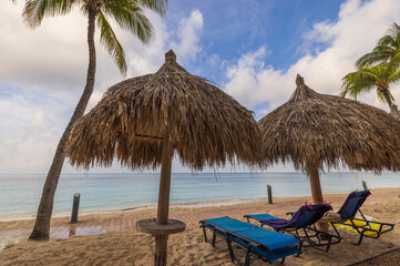 Close-up view of sun loungers with sun umbrellas on white sandy beach of Aruba island in Atlantic Ocean.