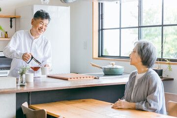 家のキッチンでコーヒーをいれる高齢者女性と高齢者男性（老夫婦）
