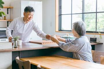 家のキッチンでコーヒーをいれる高齢者女性と高齢者男性（老夫婦）
