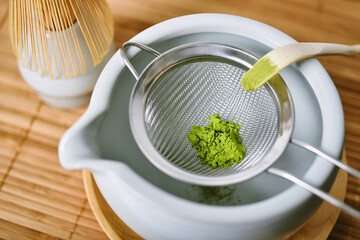Matcha tea powder in sieve on white clay tea bowl, Matcha bamboo whisk and accessories, Green tea making set, Japanese ceremony traditional drink.