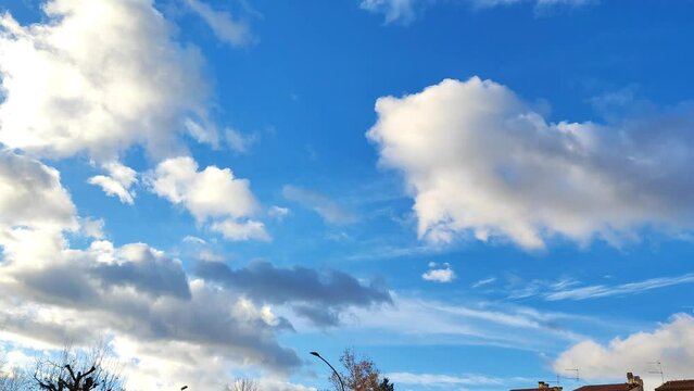 Beattiful white and gray clouds in a blue winter sky above a town neighborhood, with roooftops below. Real time. 