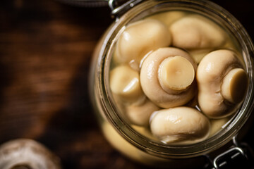 A small glass jar with pickled mushrooms on the table. 