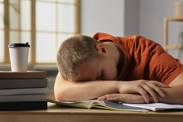 Obraz premium Tired man sleeping near books at wooden table indoors