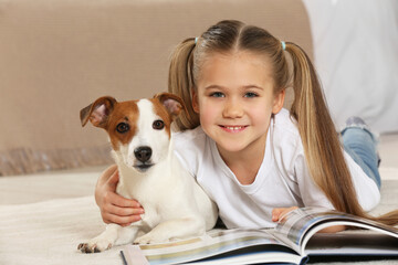 Cute girl reading book on floor with her dog indoors. Adorable pet