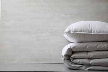 Soft folded blanket and pillow on light grey table, closeup. Space for text
