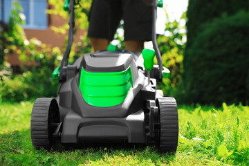 Man cutting grass with lawn mower in garden on sunny day, closeup