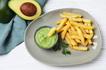 Plate with french fries, guacamole dip, parsley and avocado served on white wooden table, top view