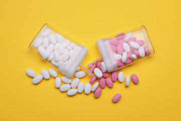 Containers and different dragee candies on yellow background, flat lay