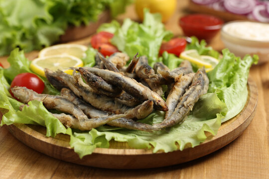 Delicious fried anchovies served with lemon, tomatoes and lettuce leaves on wooden table, closeup