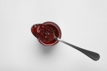 Spoon with tasty canned raspberry jam on jar against white background, top view