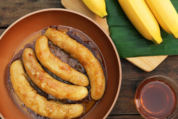 Delicious fresh and fried bananas with rum on wooden table, flat lay
