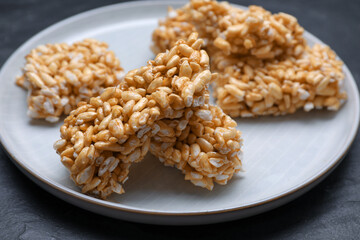 Plate with puffed rice pieces (kozinaki) on black table, closeup