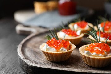 Delicious tartlets with red caviar and cream cheese served on wooden table, closeup
