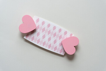 two wooden hearts painted pink clipped to a cut paper card with diamond or square pattern