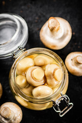 Delicious pickled mushrooms in a small glass jar on the table. 