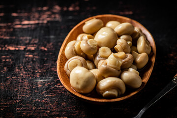 Pickled mushrooms in a wooden plate on the table. 