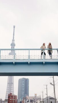 4K Happy Asian woman friends walking on overpass bridge for crossing city street together in Tokyo city, Japan in the morning. Attractive girl enjoy and fun outdoor lifestyle travel on winter vacation
