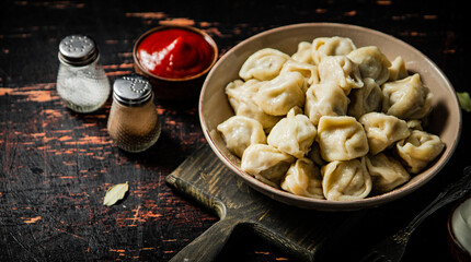 Dumplings in a plate on a cutting board with tomato sauce and sour cream. 