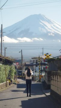 Asian woman enjoy outdoor lifestyle using mobile phone taking picture of mt Fuji covered with snow and local train running cross the street during travel small town in Japan in autumn holiday vacation