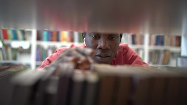 Unhappy stressed African American guy student looking for book on library shelf, stuck on dissertation or research project, having problem finding textbook. Effective literature searching, education