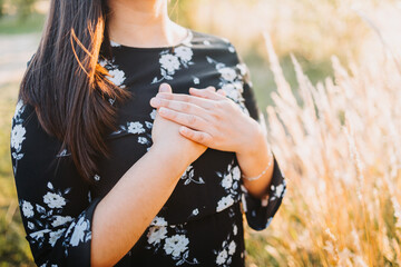 Hopeful woman putting hands on her chest in gratitude for God's blessings, in the field. Copy space