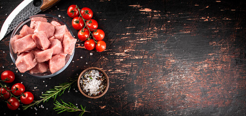 Pieces of raw pork in a glass bowl with tomatoes and rosemary. 