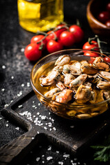 Pickled mussels in a bowl on a cutting board with cherry tomatoes. 