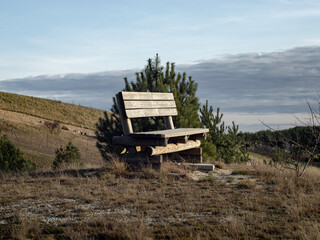 Naklejka premium Empty park bench on top of a hill in the nature. The calm and idyllic landscape is in the background. Nice place to rest in a rural area without people.